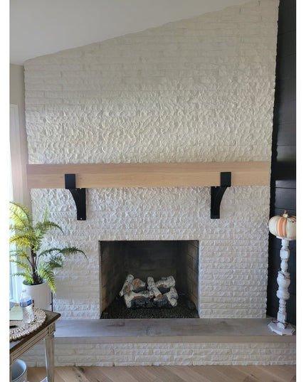 Black metal Seneca 3" farmhouse mantel brackets supporting natural wood beam on white painted brick fireplace by Industria...