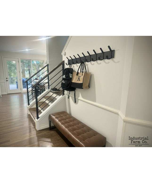 Riseform black metal wall mounted coat rack with multiple hooks installed in modern entryway with brown leather bench and ...