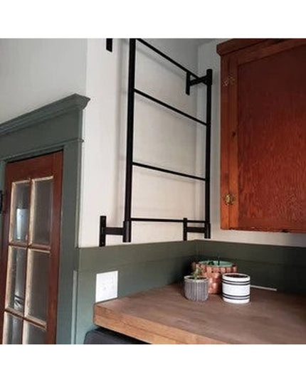Black metal Wall Mounted Ossit Ladder by Industrial Farm Co displayed in rustic kitchen with green cabinets and wood count...