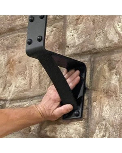 Black steel Spafford 3-inch mantel bracket with decorative rivets mounted on stone wall, hand demonstrating size - Industr...