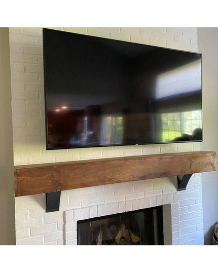 Black metal Jeffery Style Shelf Brackets supporting rustic wood mantel below wall-mounted TV above white brick fireplace