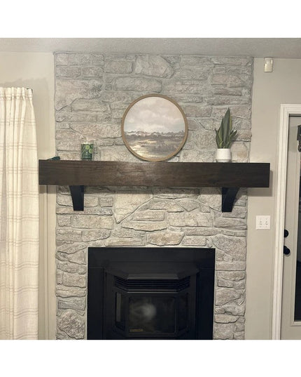 The Eleanor Minimal Steel Bracket in black supporting a dark wood mantel on gray stone fireplace with round mirror and pla...