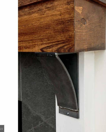 Industrial Farm Co Tipp Hill black metal mantel support bracket holding rustic wood beam mantel against white wall