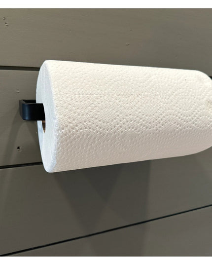 The Jordan Paper Towel Holder by Industrial Farm Co mounted on gray shiplap wall with white paper towel roll and black met...