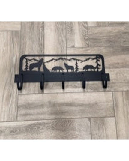 Black metal wolf silhouette coat rack with mountain forest scene design and 5 hooks mounted on light wood parquet floor